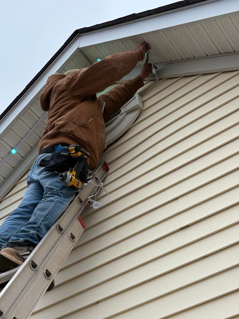 Worker on a ladder fixing the roof gutter on a beige house
