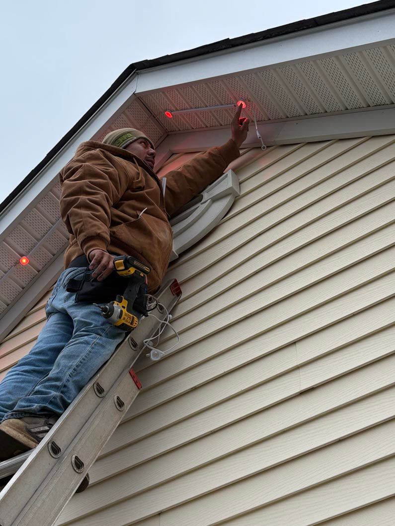 Worker on a ladder installing red lights under a roof eave