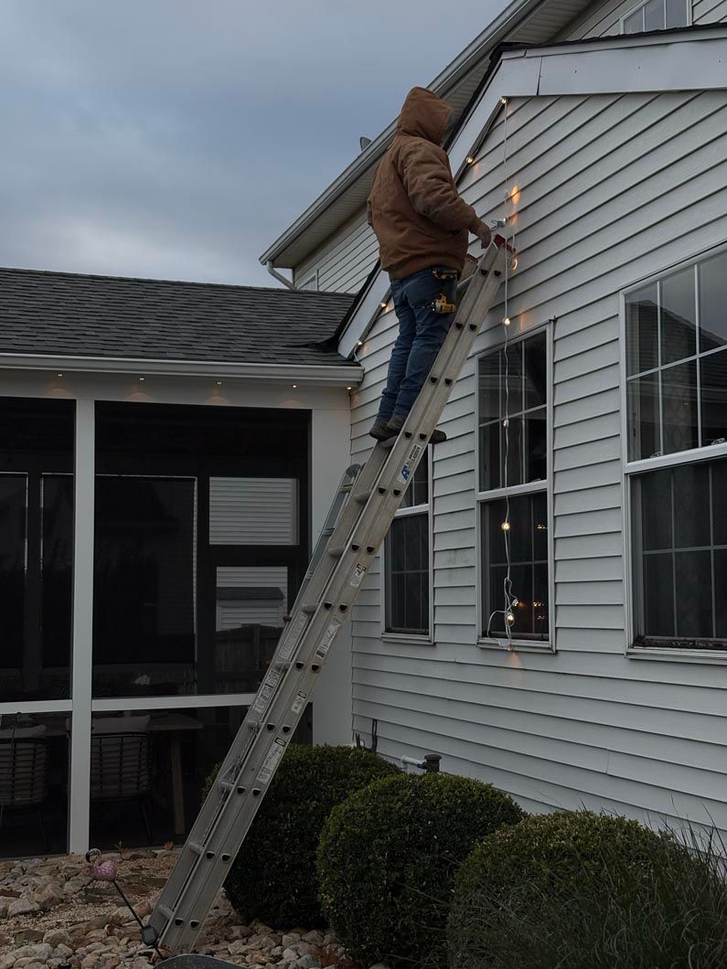 Person on a ladder painting a white house exterior near a window