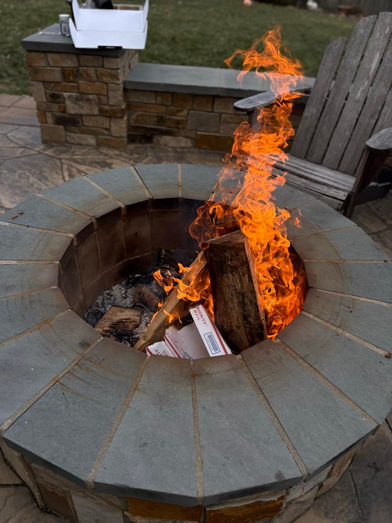 Stone fire pit with bright flames burning in a backyard patio area