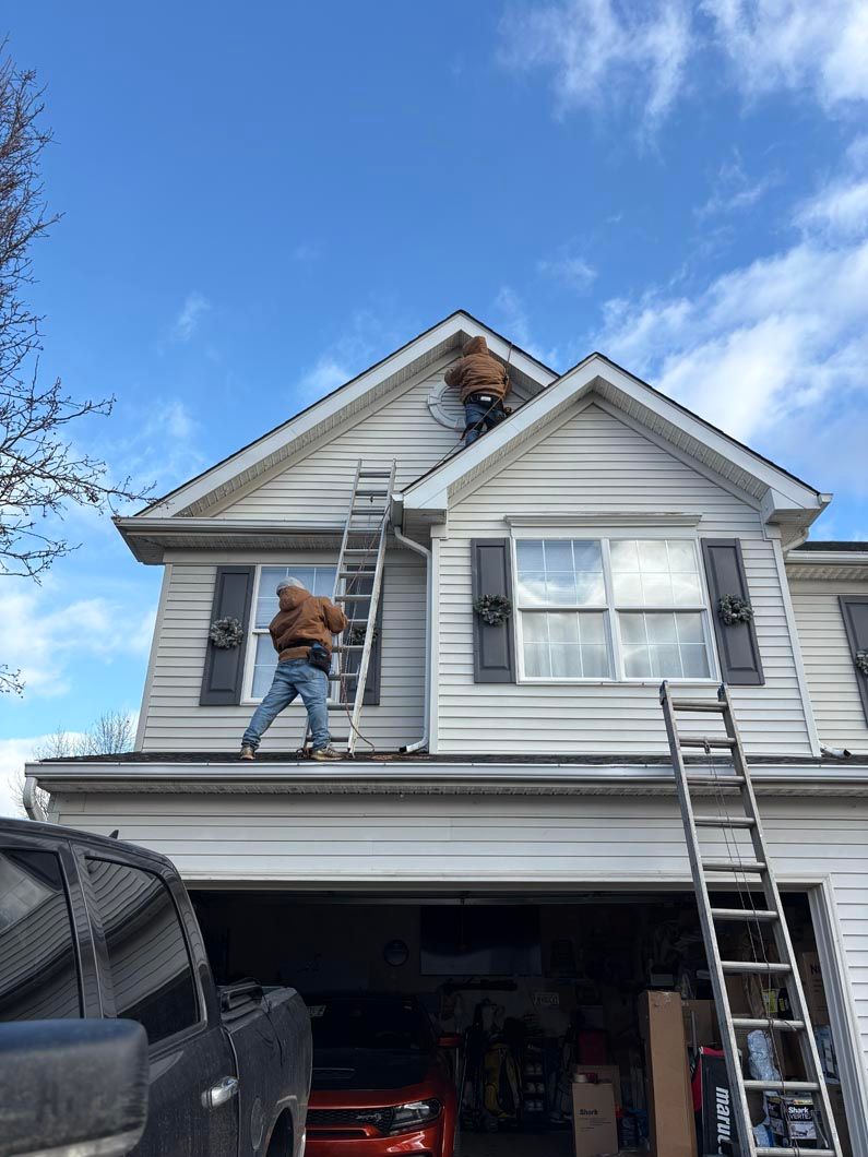 Worker on ladder repairing the roof of a white house over a garage under a blue sky