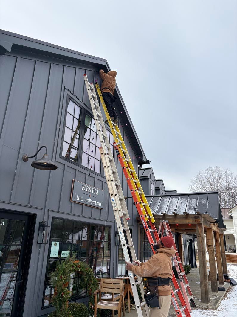 Worker uses a long ladder to inspect a roof on a gray building.