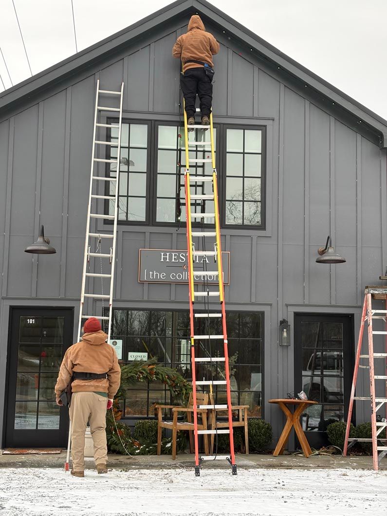 Workers on ladders painting the gray exterior of a building with tall windows.