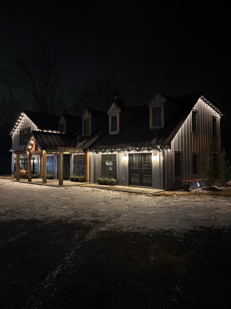 Snowy house exterior at night with warm porch lights and a dark sky