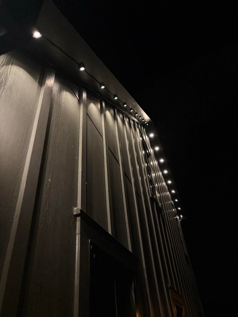 Nighttime exterior of a building with vertical siding and string lights along the roofline