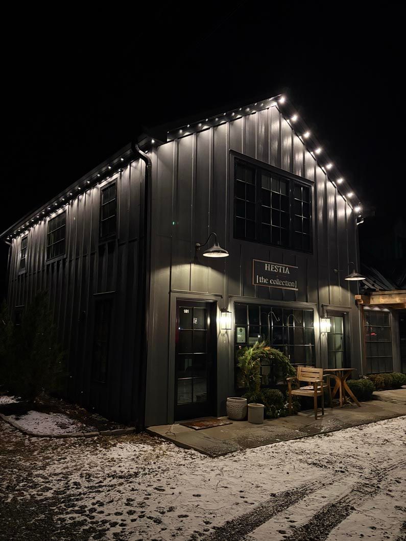 Snow-dusted black building at night with string lights along the roofline and a warmly lit entrance