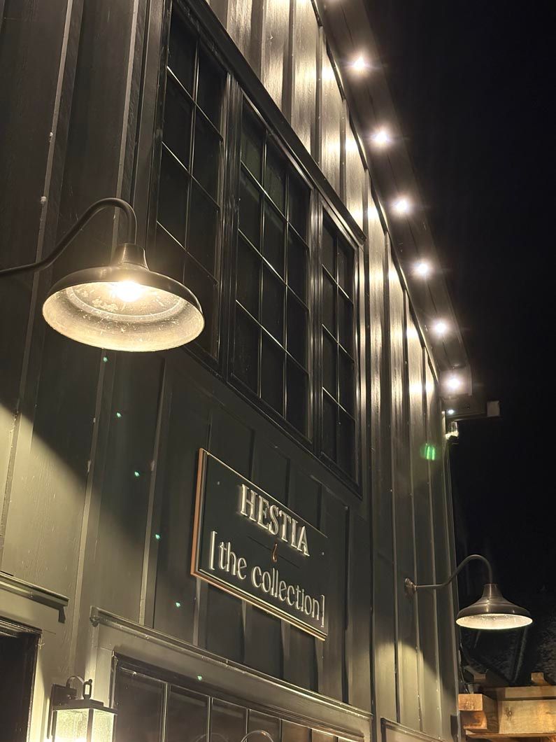 Nighttime view of a black building facade with lit signs and hanging industrial lamps