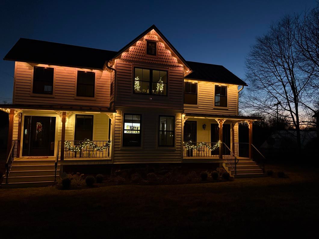 Lit two-story house with warm porch lights at dusk against a dark blue sky