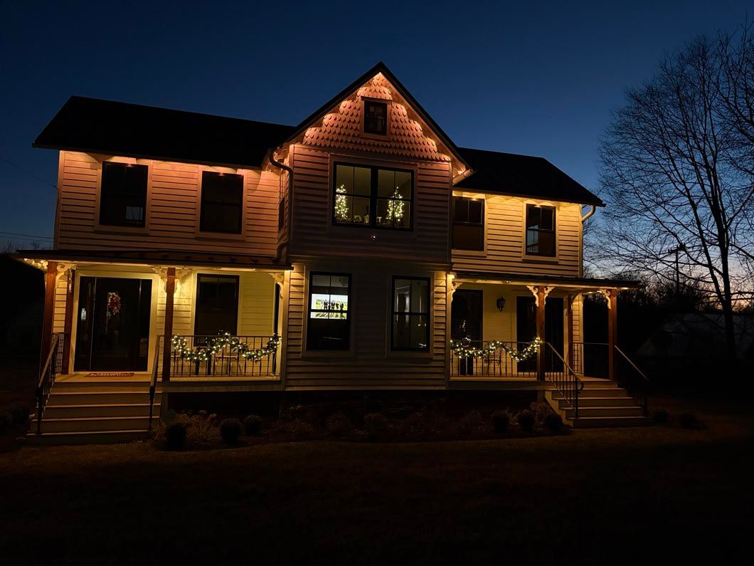 Lit wooden house at dusk with warm porch lights and dark blue sky