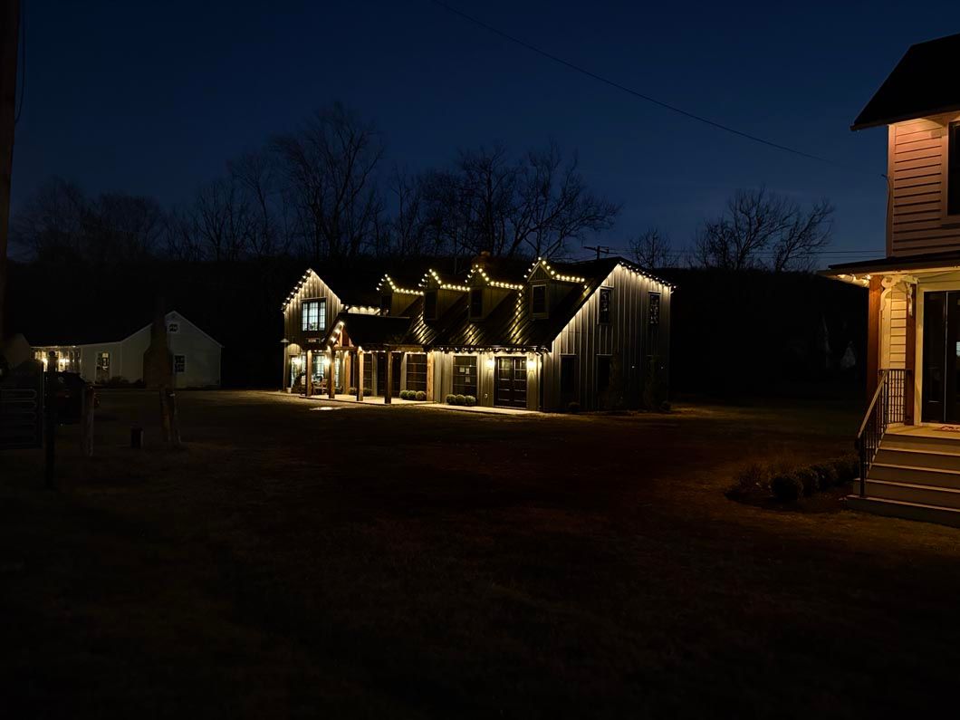 House lit with warm holiday lights at dusk, with a dark sky and neighboring homes in the background