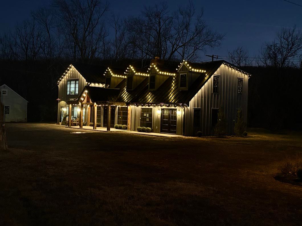 House outlined with warm white Christmas lights at night, glowing against a dark yard and sky