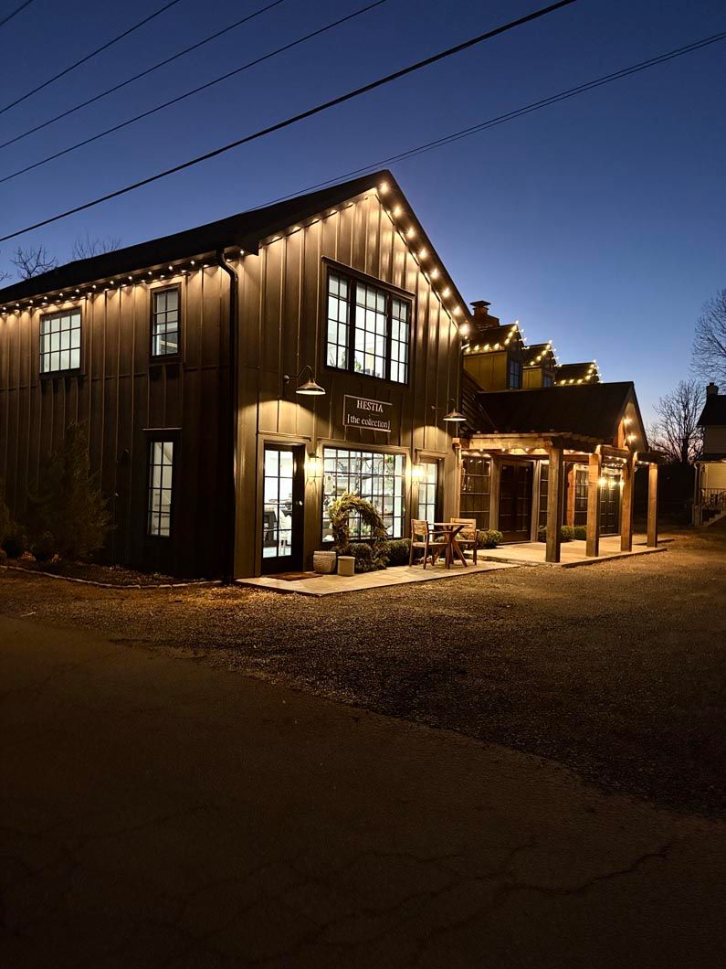 Lit wooden house at dusk with warm lights, large windows, and a gravel driveway