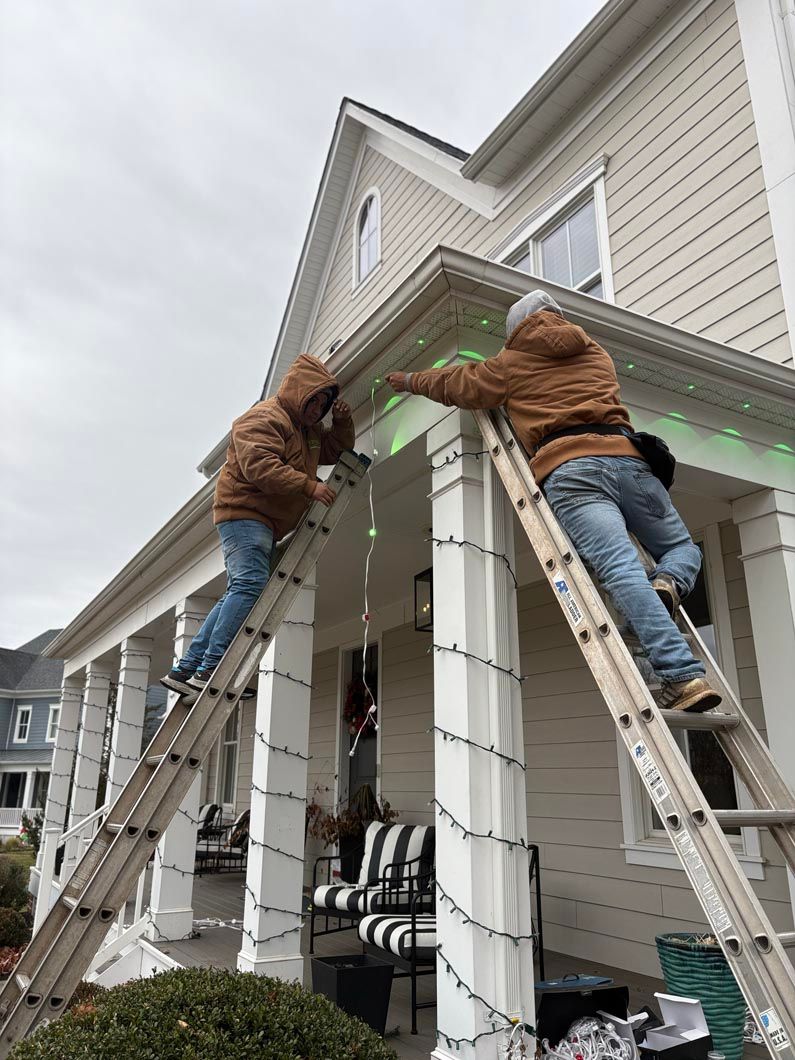 Two workers on ladders installing white trim on a house porch roof