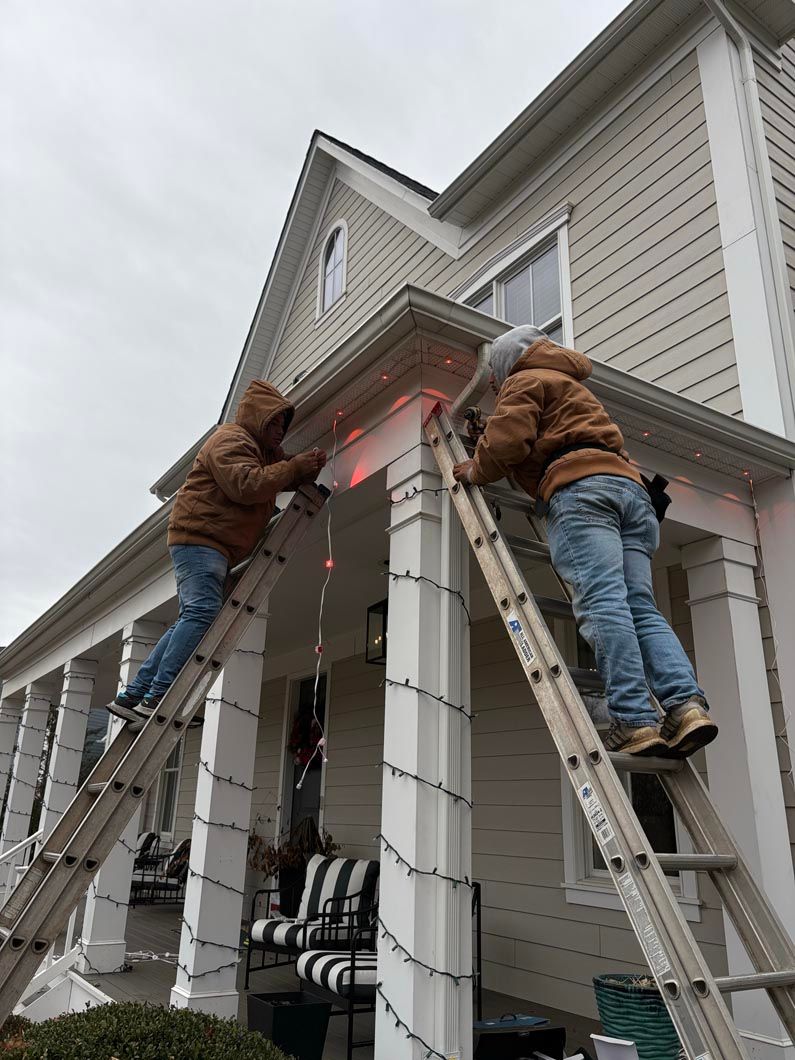 Two workers on ladders painting a house exterior under gray skies