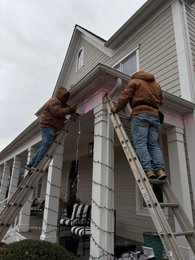 Two workers on ladders painting a house porch with pink trim