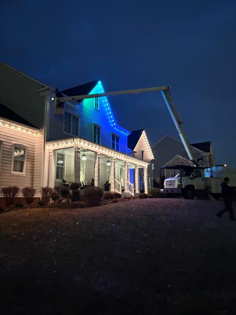 Nighttime view of a house with blue holiday lights and a lit porch, with a crane parked in the driveway.