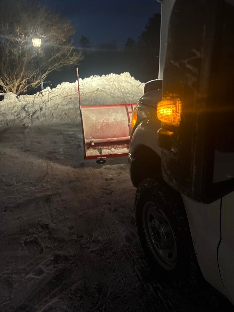 Pickup truck with lit amber light beside a red trailer loaded with snow at night