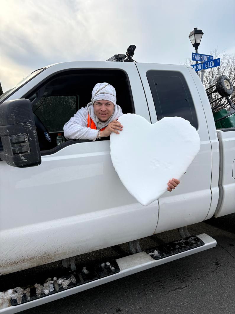 Person leaning out of a white pickup truck, holding a large white heart in snowy weather.