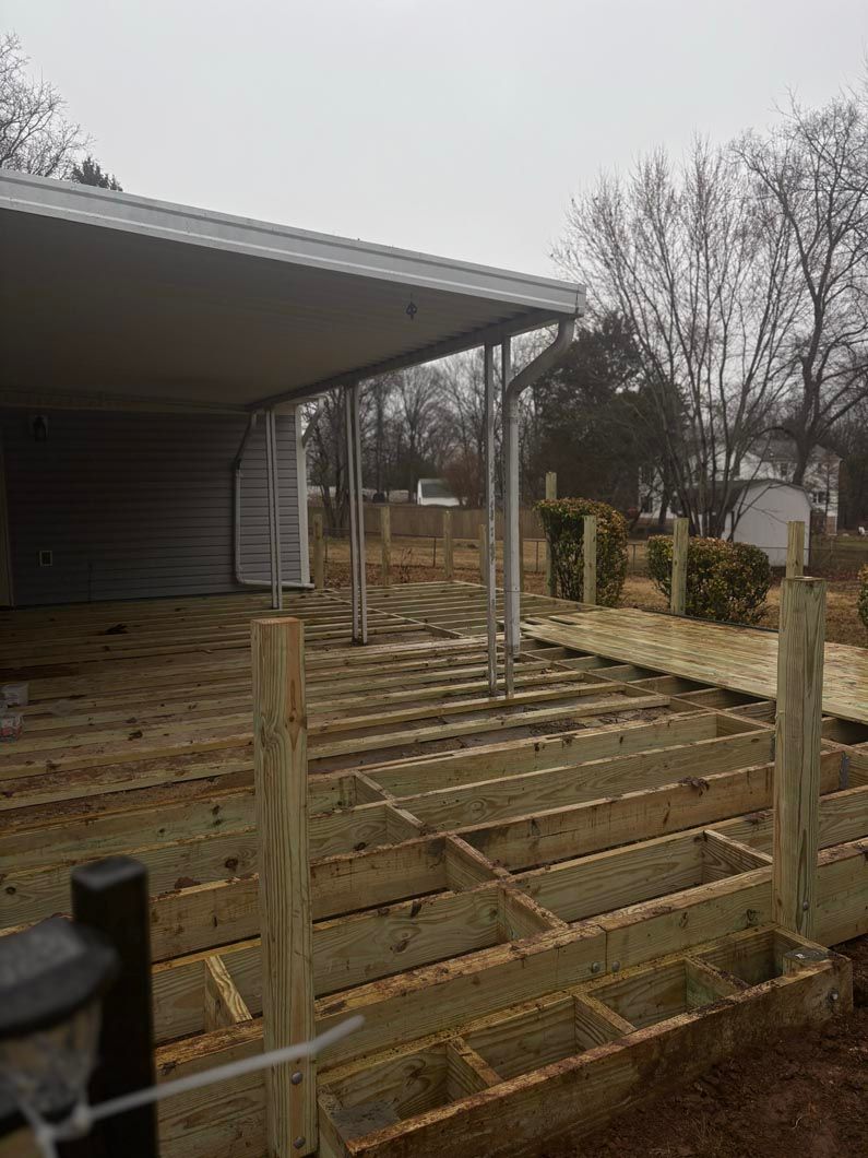 Covered wooden deck with railing posts and a corrugated roof beside a yard on a cloudy day