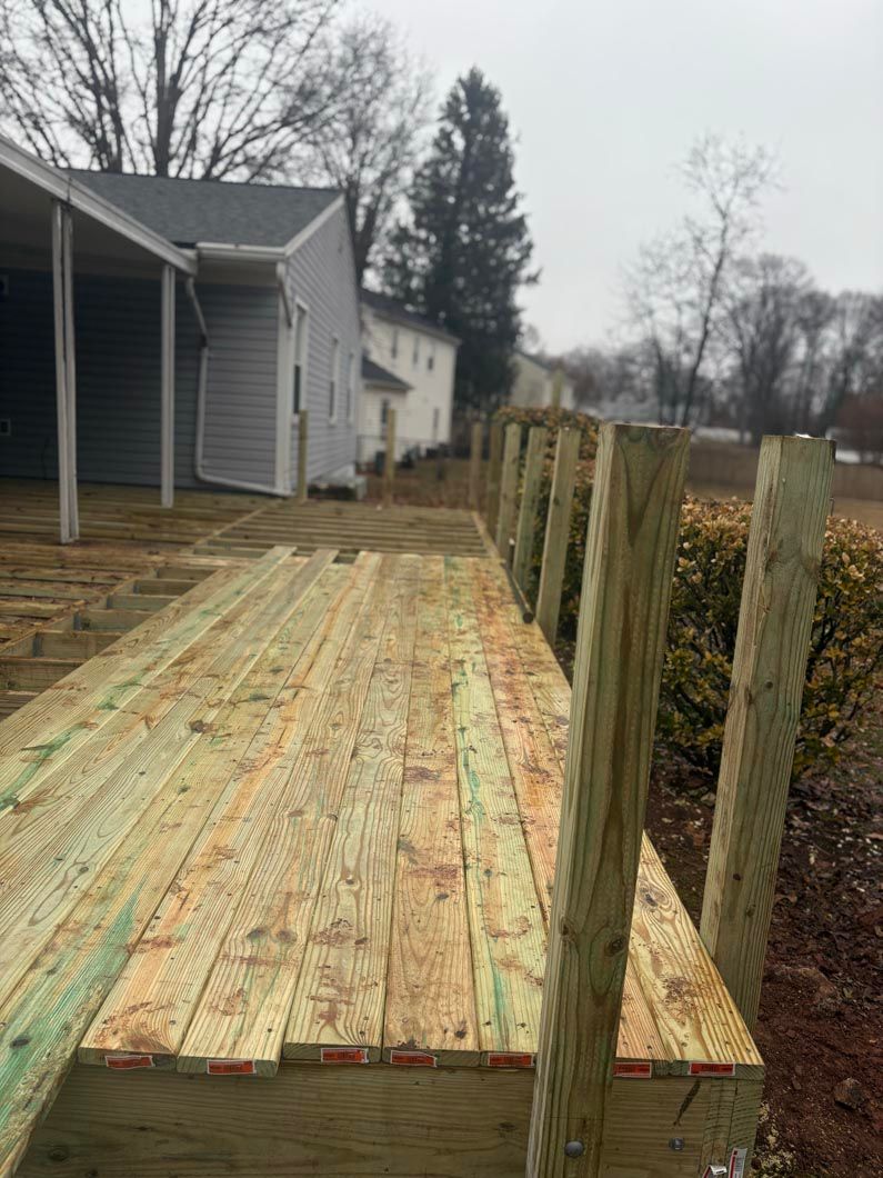 Wooden deck under construction beside a gray house, with fence posts along the right side.