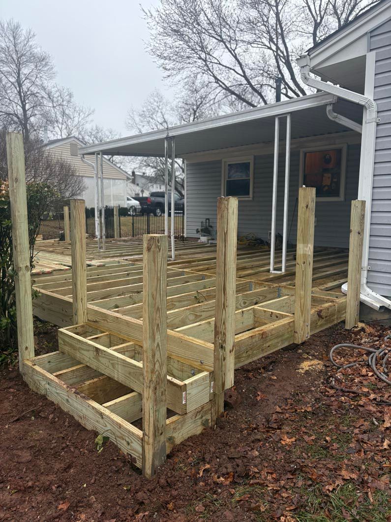 Unfinished wooden wheelchair ramp and porch deck beside a gray house on a rainy day