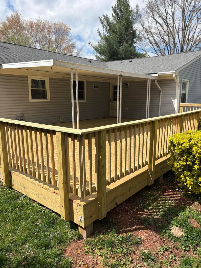 Wooden deck with railing attached to a gray house, viewed from the backyard.