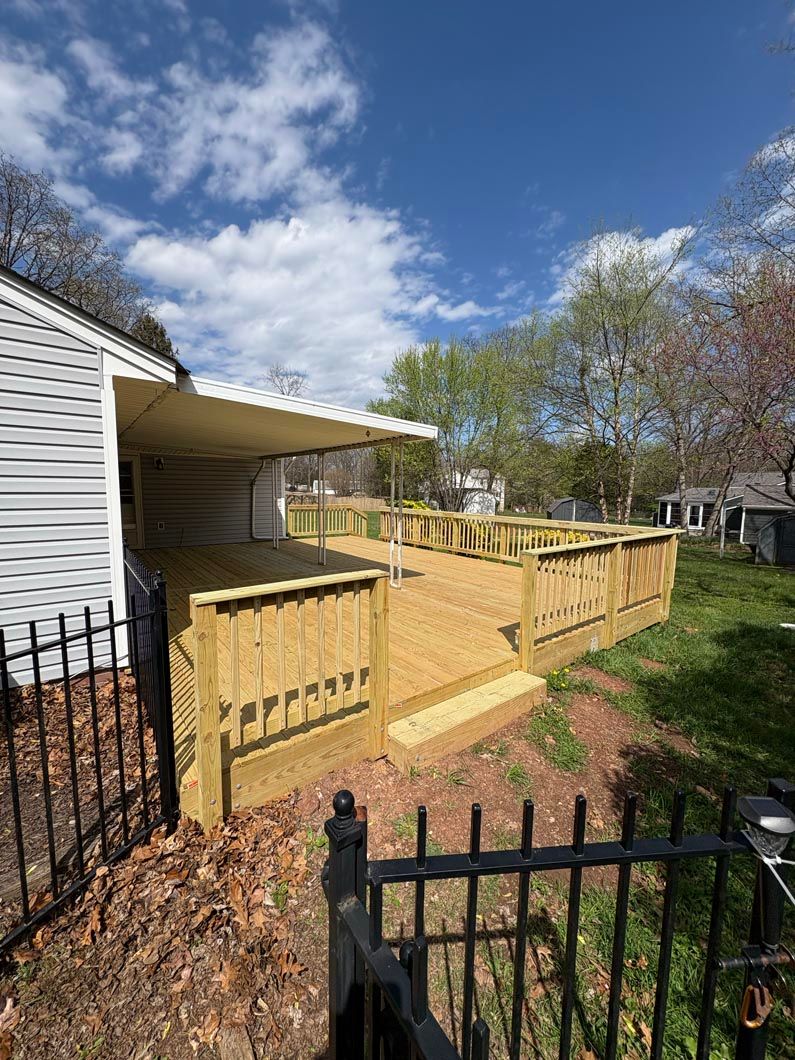Wooden deck with railings beside a white house, overlooking a grassy yard under a partly cloudy sky