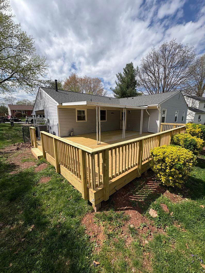 Backyard deck with wooden railing beside a beige house, surrounded by trees and shrubs.