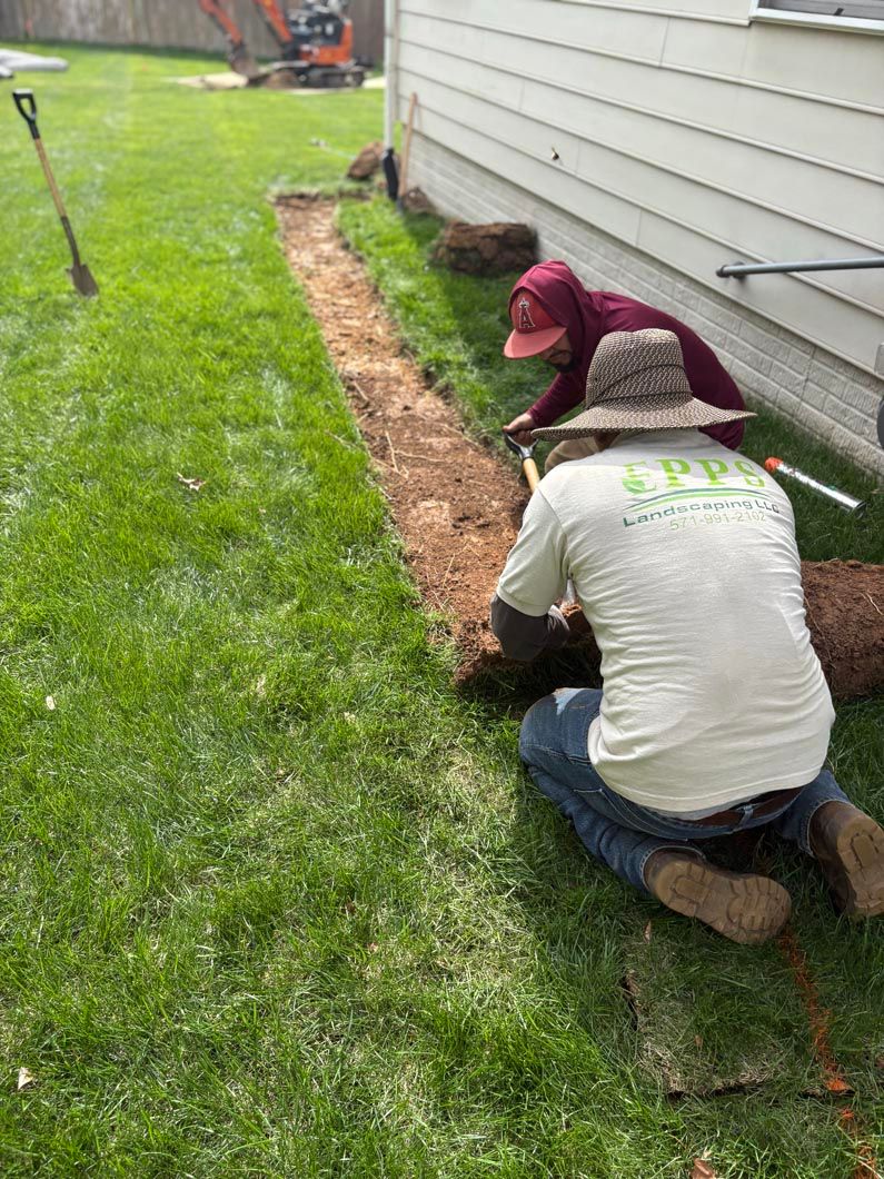 Two workers laying mulch along the side of a house beside a green lawn.