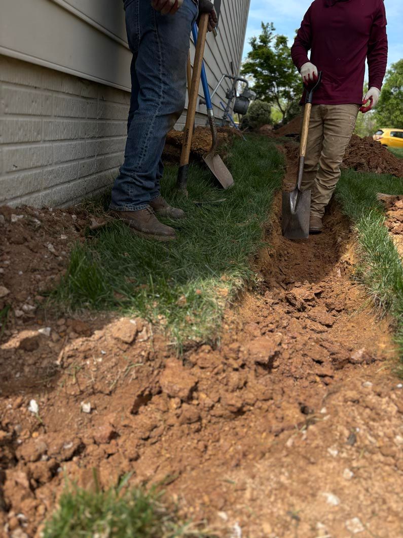 Two people digging a trench beside a house, with a shovel and muddy soil.