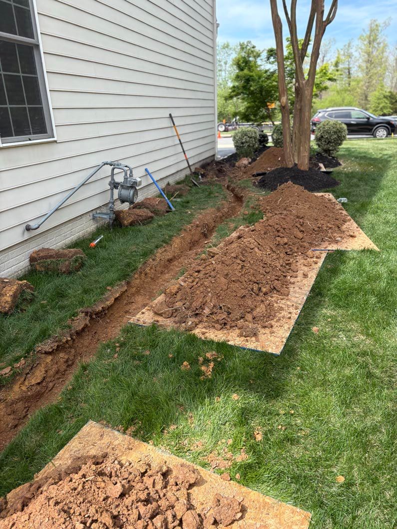Backyard landscaping with a tree, fresh soil trench, and mulch beside a house under repair