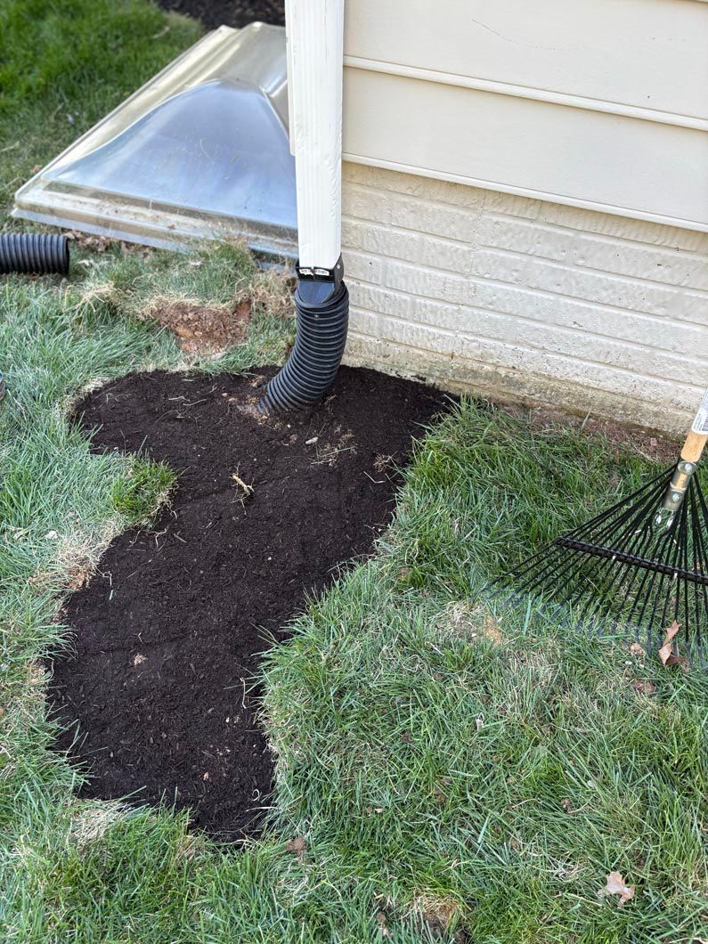 Fresh dark soil piled around a downspout beside a house wall and lawn