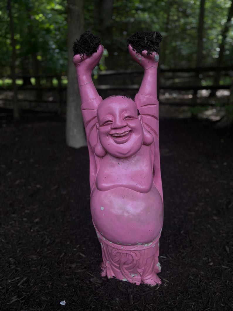 Pink smiling statue with arms raised in a dark outdoor setting
