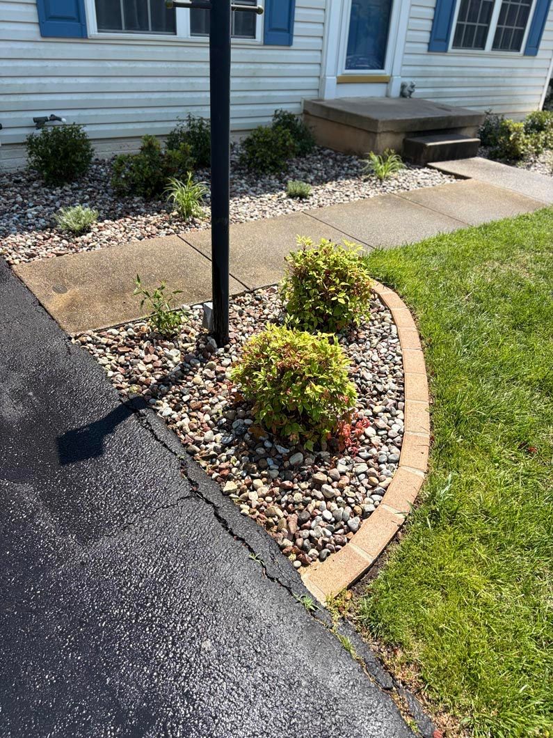 Front walkway with curved stone border, gravel bed, shrubs, and a black lamp post by a house entrance