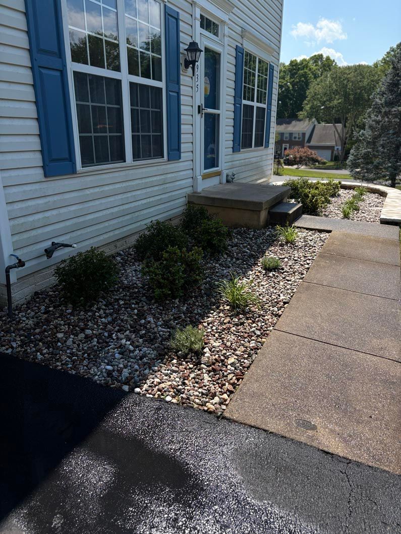 House exterior with blue shutters, a concrete walkway, and landscaped stone mulch beds along the wall