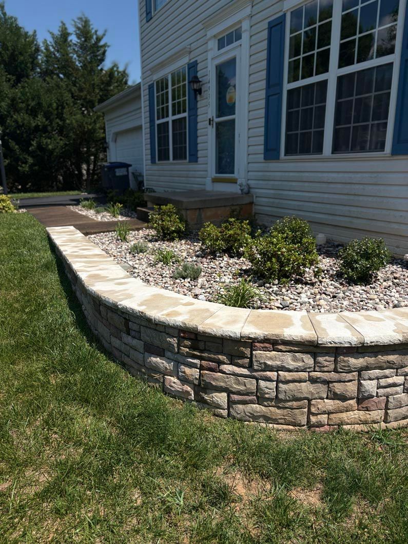 Curved stone retaining wall beside a house with white windows and a landscaped flower bed