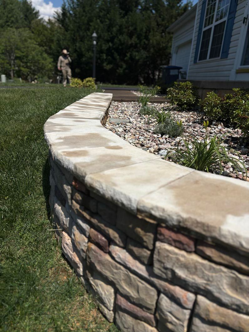 Curved stone retaining wall beside a house, with a landscaped garden and lawn.