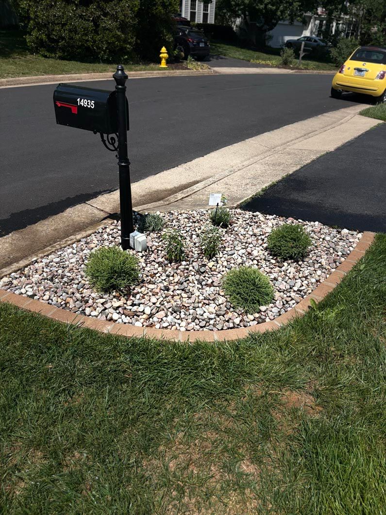 Mailbox beside a small rock garden in a suburban driveway, with a yellow car in the background.