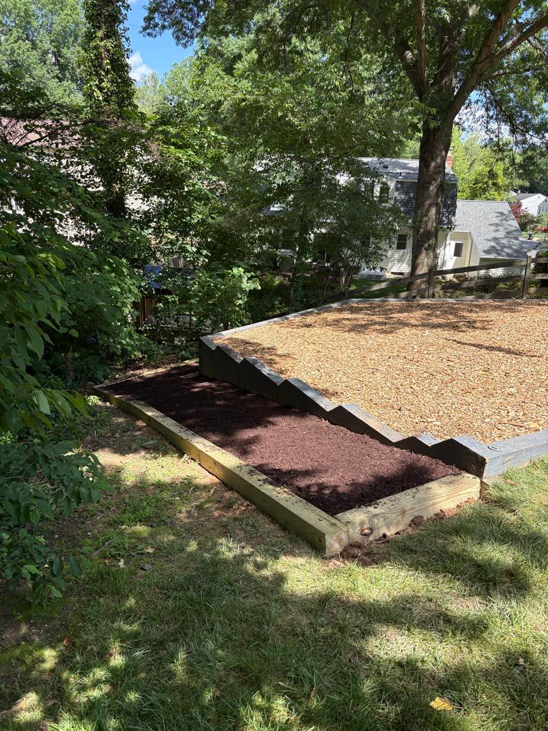 Small landscaped garden bed with fresh dark soil beside a grassy yard and trees outdoors