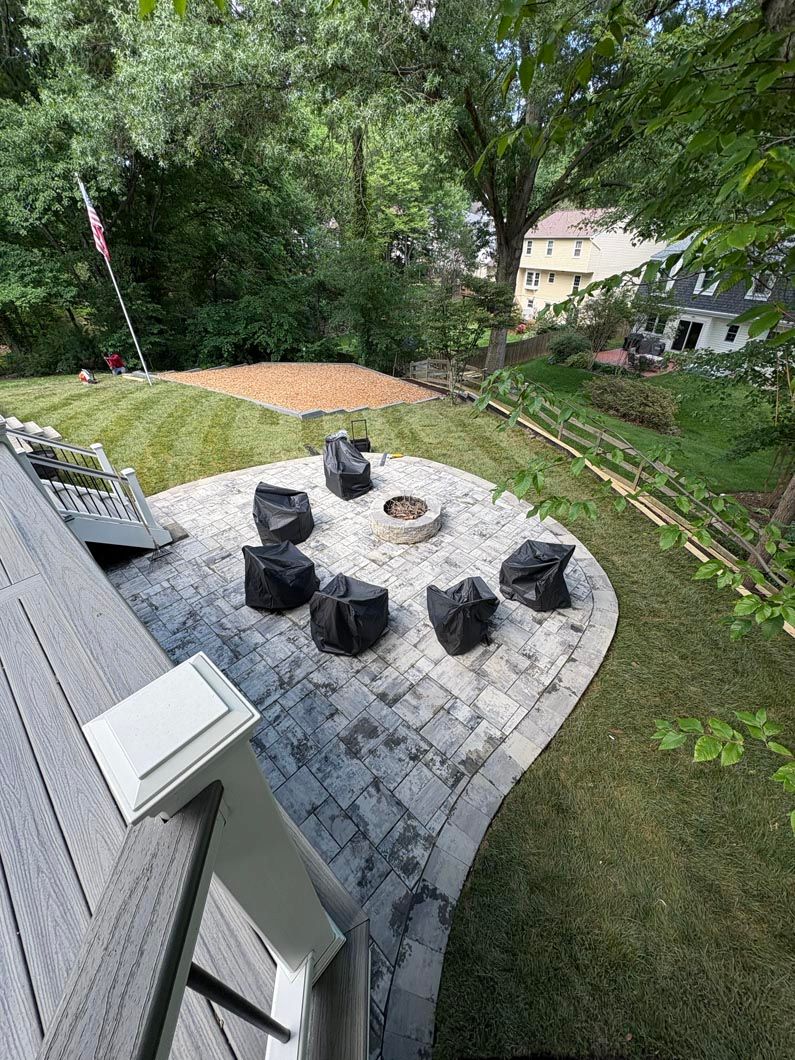 Backyard patio with six black chairs around a fire pit, surrounded by trees and grass.