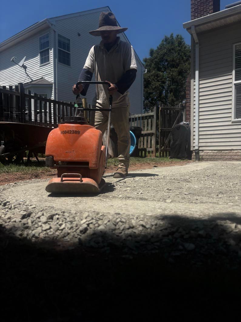 Person using a concrete mixer on a gravel driveway between two houses