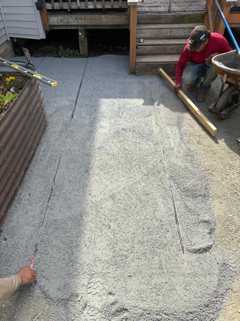 Workers pouring and smoothing concrete in a backyard patio area