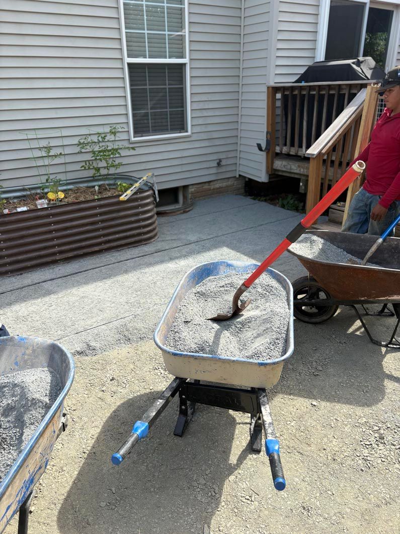 Person shoveling gravel into a wheelbarrow in a backyard beside a house