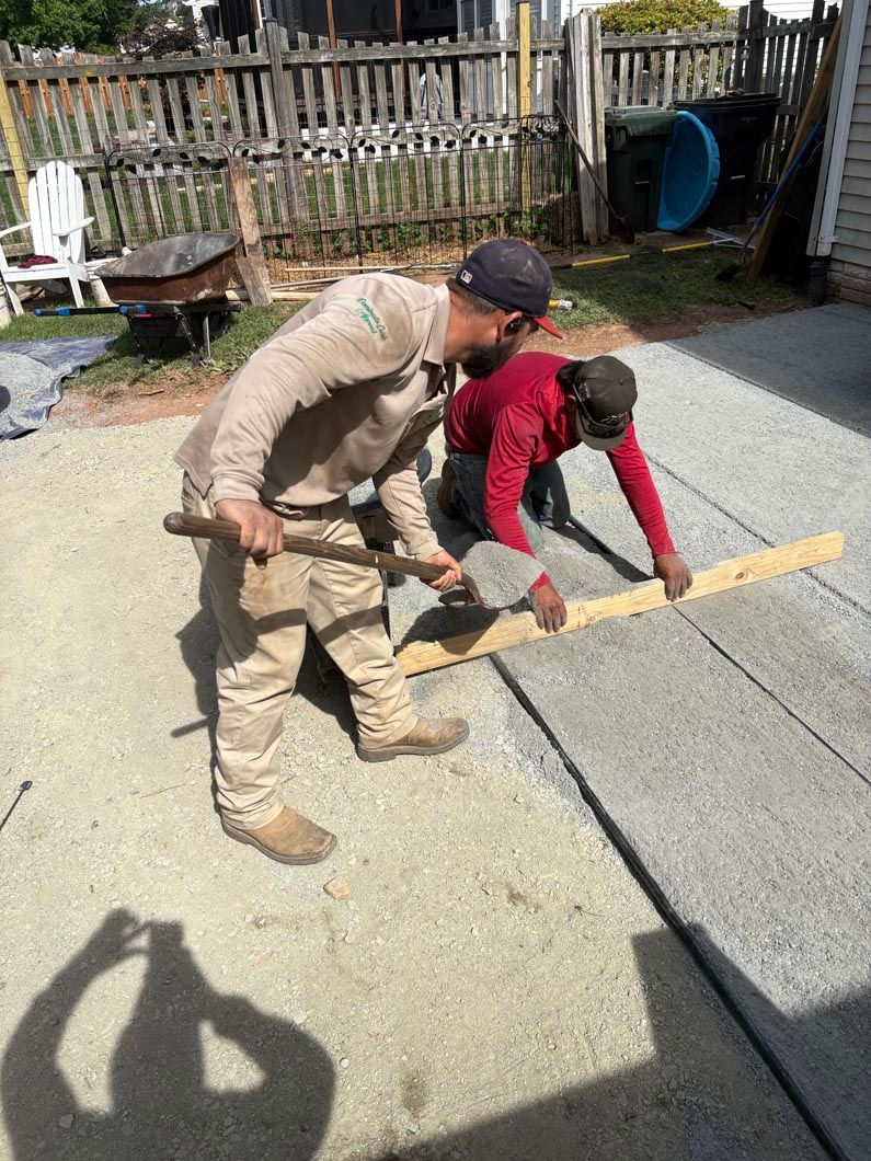 Two people working together to lift a long wooden beam in a gravel yard.