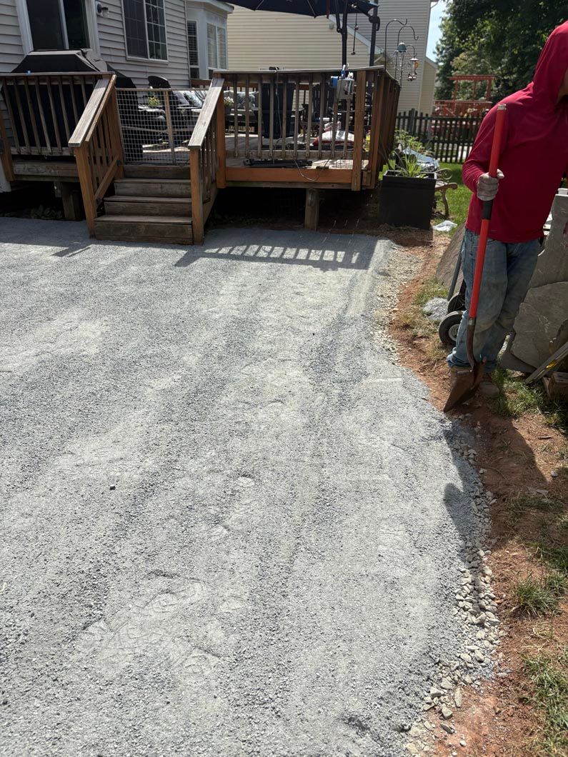 Gravel driveway leading to a wooden deck, with a person in a red jacket standing at right.