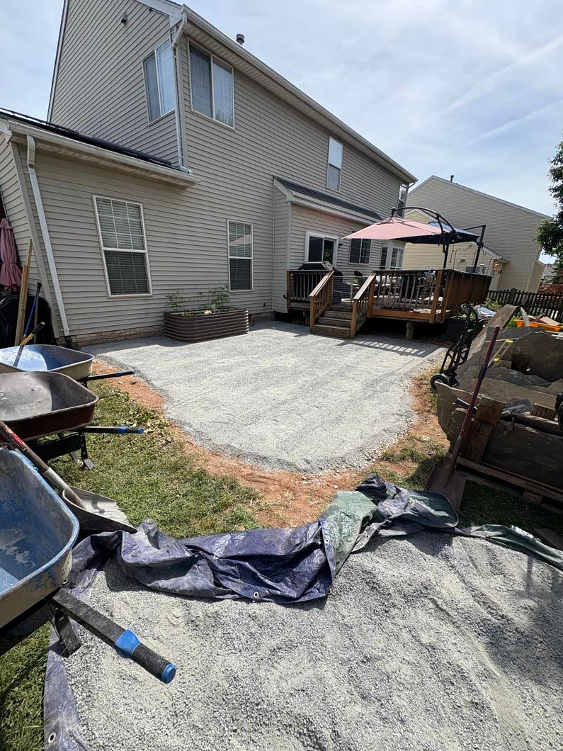 Backyard with gravel and debris beside a beige house, showing storm damage and a deck with an umbrella.