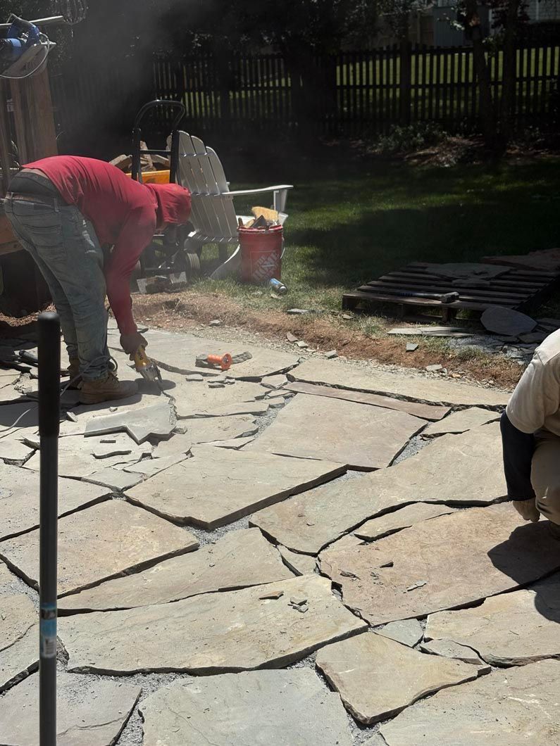 Two workers laying large stone pavers in a sunny backyard patio.