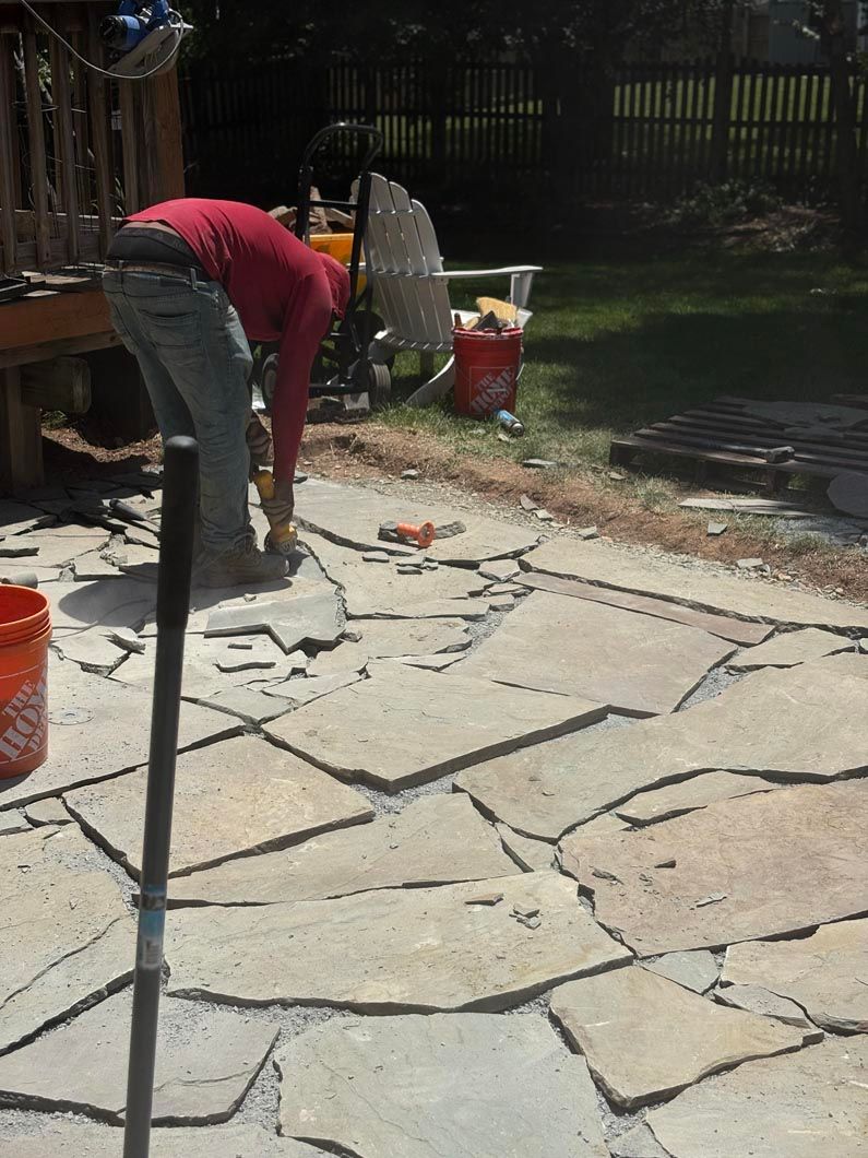 Worker in red shirt paving cracked concrete patio with a jackhammer outdoors