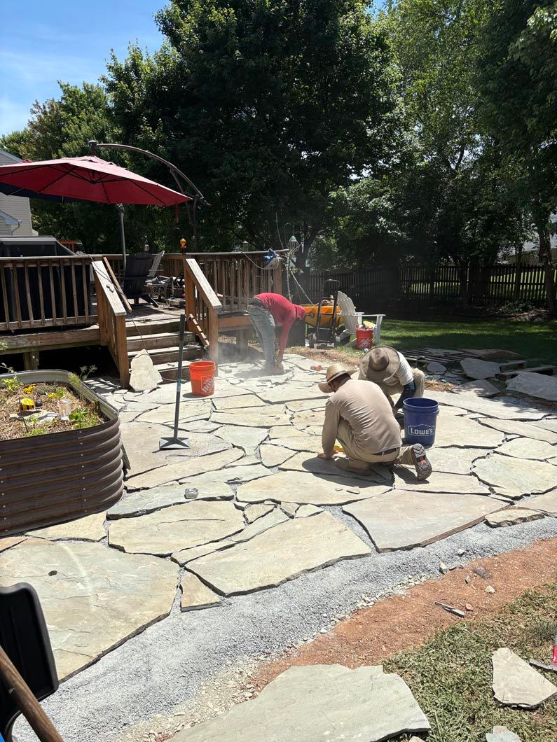 Children playing with water on a stone patio beside a wooden deck and trees in a sunny backyard