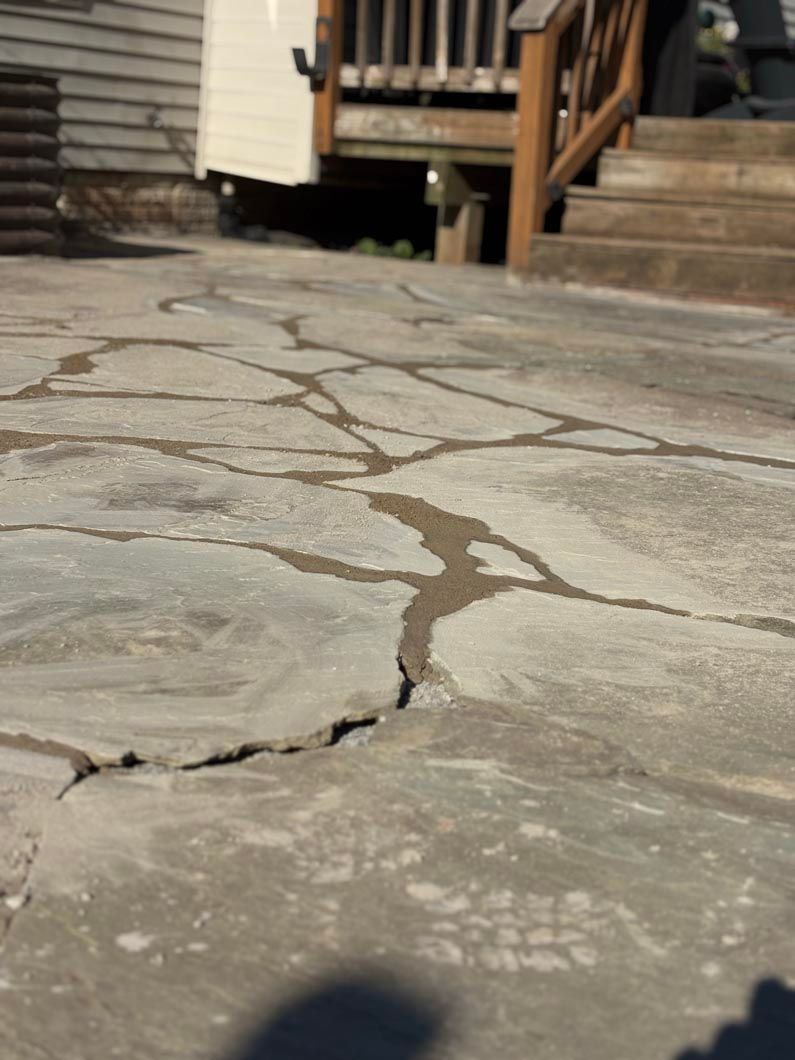 Cracked concrete walkway leading to wooden steps and porch in the background